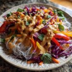 Vibrant Spring Roll Bowl with Peanut Sauce drizzled over rice vermicelli noodles, shredded cabbage, and bell peppers.