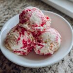 Three scoops of creamy Strawberry Banana Ice Cream with bright red strawberry swirls in a white bowl.