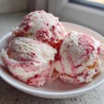 Three scoops of creamy Strawberry Banana Ice Cream swirled with bright red strawberry puree in a white bowl.