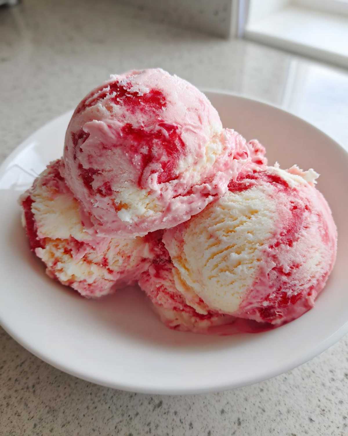Three scoops of marbled pink and white Strawberry Banana Ice Cream served in a small white bowl.