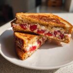 Two halves of golden-brown Strawberry Cream Cheese Stuffed French Toast stacked on a white plate.