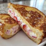 Two halves of golden-brown Strawberry Cream Cheese Stuffed French Toast dusted with powdered sugar.