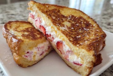 Two halves of golden-brown Strawberry Cream Cheese Stuffed French Toast dusted with powdered sugar.