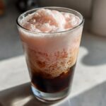 Close-up of Strawberry Cream Cold Brew showing dark coffee layered beneath thick, pink, frothy strawberry cream topping.