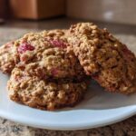 A stack of golden brown Strawberry Oatmeal Breakfast Cookies with visible oats and pieces of red strawberry on a white plate.