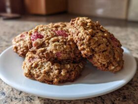 A stack of golden brown Strawberry Oatmeal Breakfast Cookies with visible oats and pieces of red strawberry on a white plate.