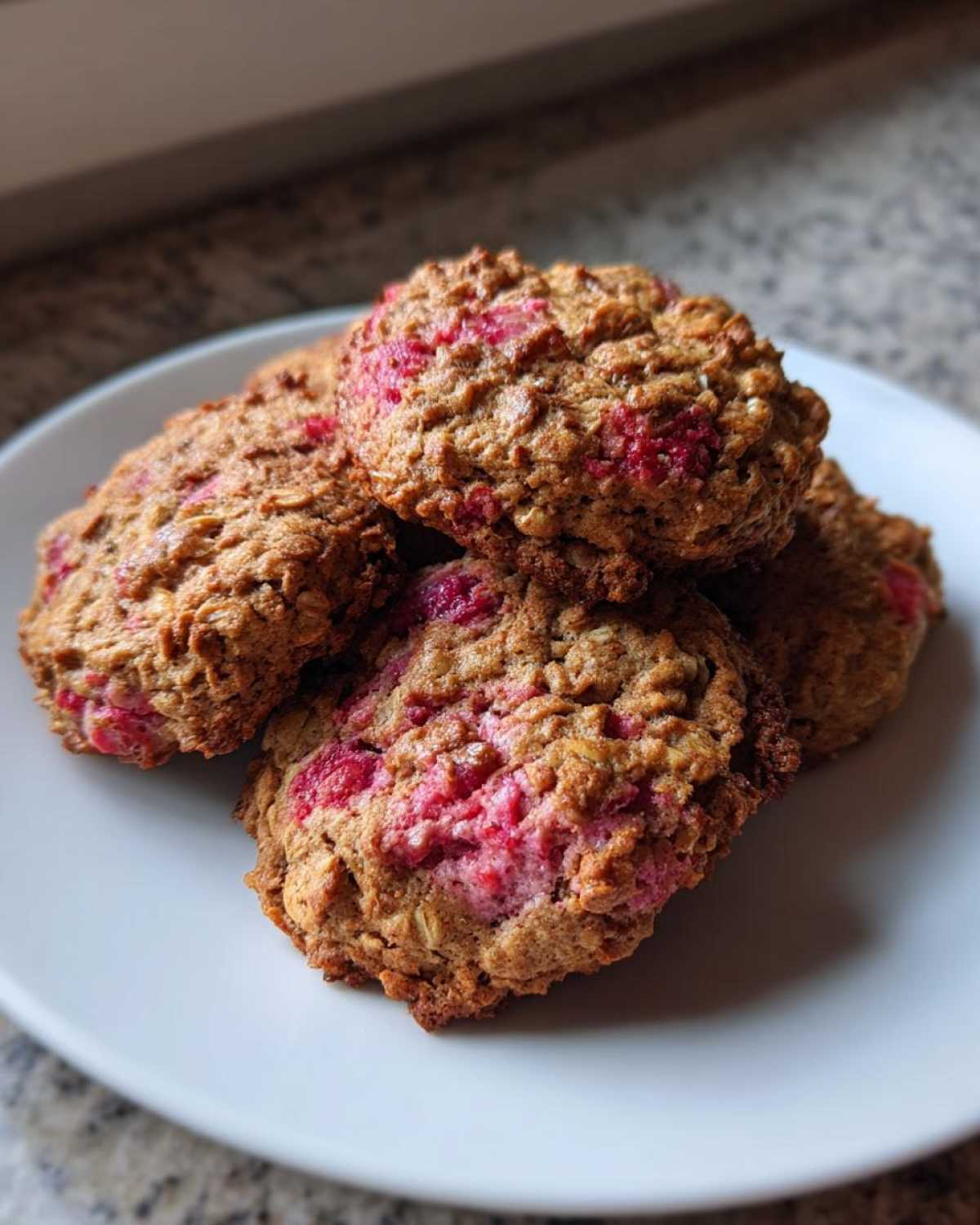 A stack of four golden brown Strawberry Oatmeal Breakfast Cookies with visible pink strawberry pieces on a white plate.