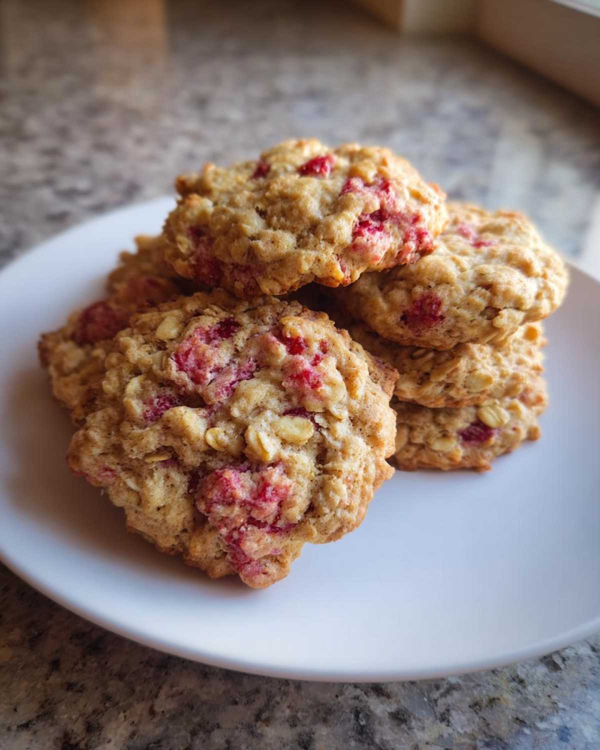 A stack of freshly baked Strawberry Oatmeal Breakfast Cookies featuring visible oats and bright red strawberry pieces.