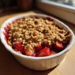 Close-up of a freshly baked Strawberry Rhubarb Crisp with a golden oat topping in a white oval dish.