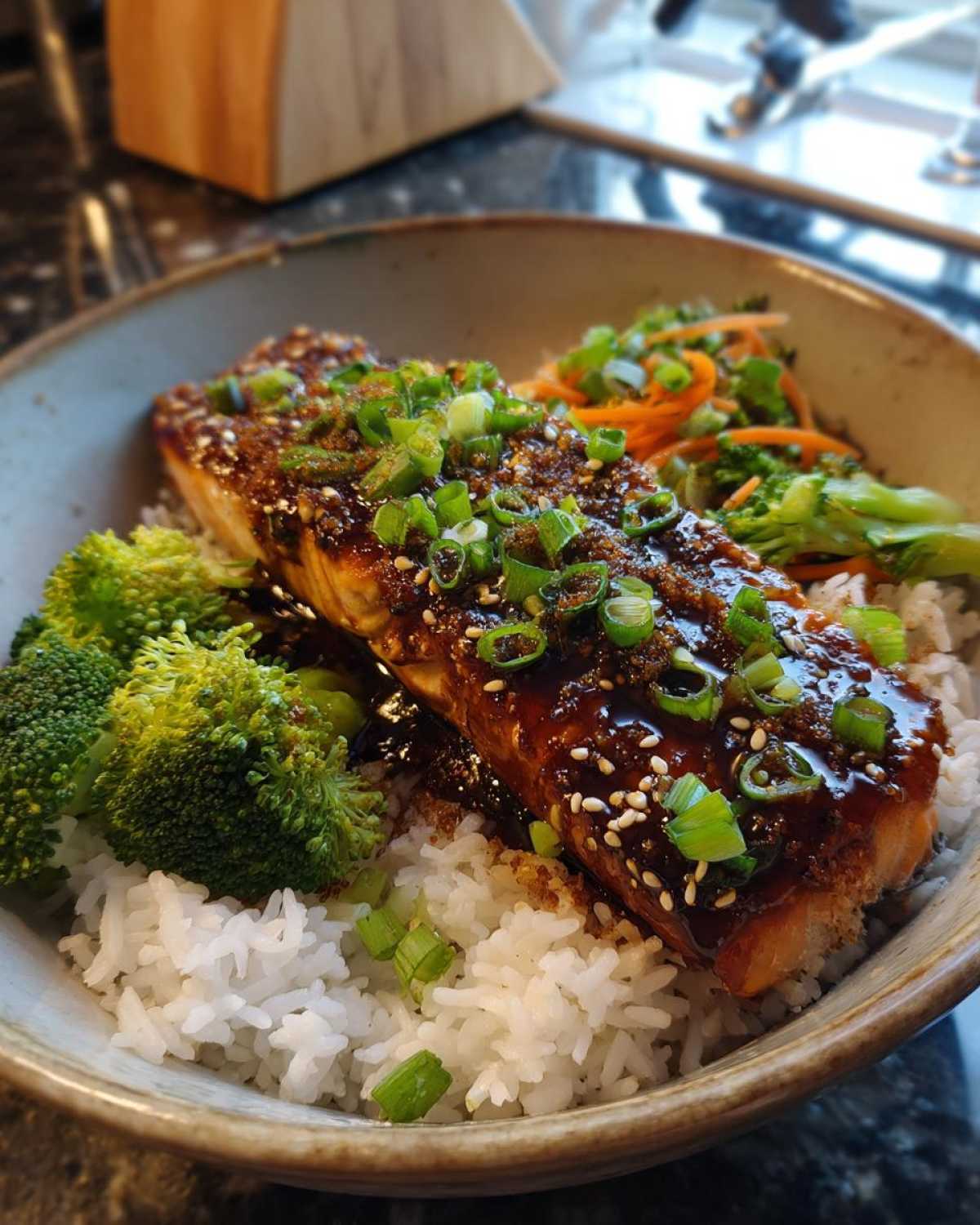 Close-up of a Teriyaki Salmon Rice Bowls featuring a glazed salmon fillet over white rice with broccoli and carrots.