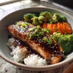 A close-up of a Teriyaki Salmon Rice Bowls featuring glazed salmon over white rice with steamed broccoli and sliced carrots.