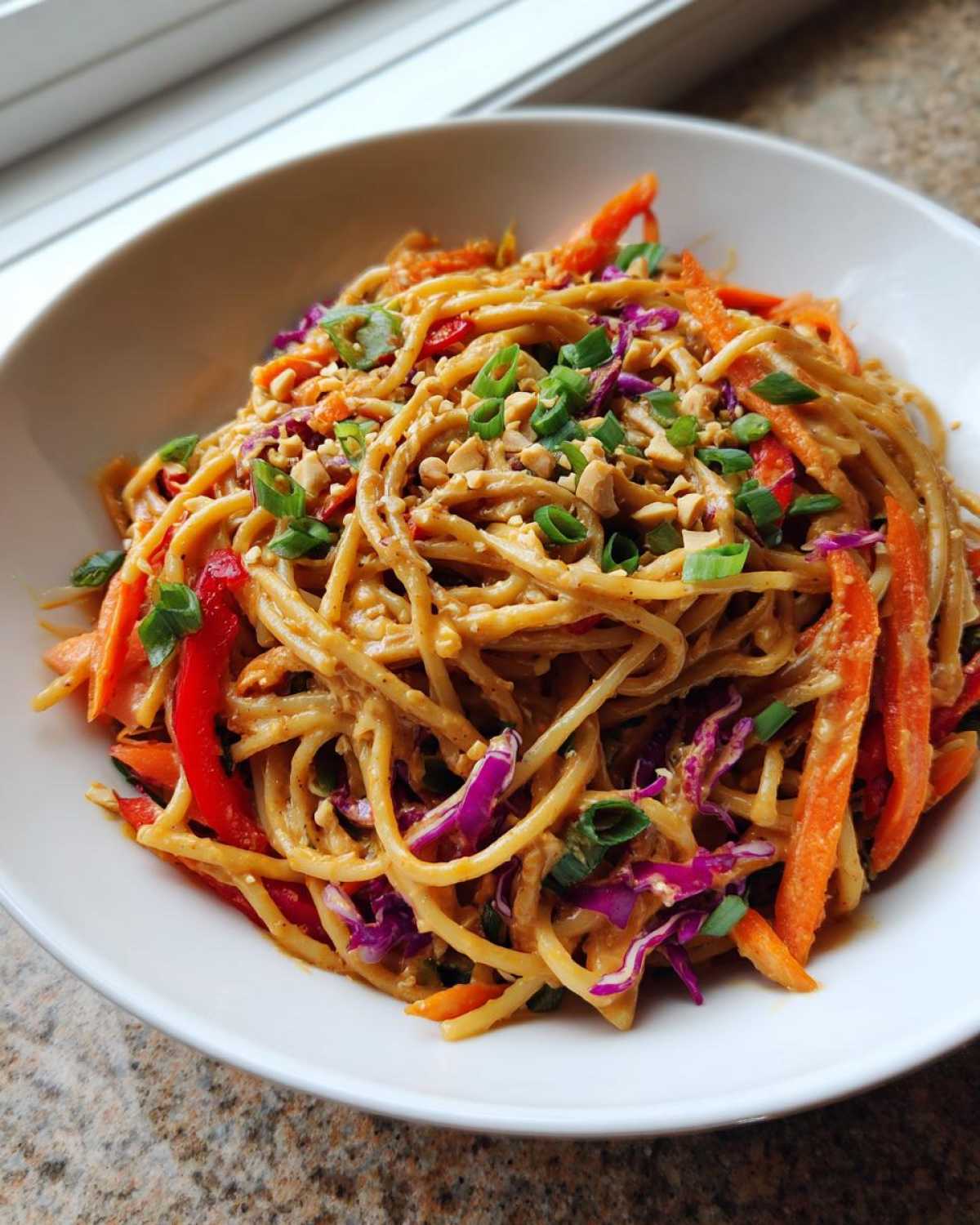 A close-up of Thai Peanut Noodles with Crunchy Veggies coated in peanut sauce, topped with peanuts and green onions.