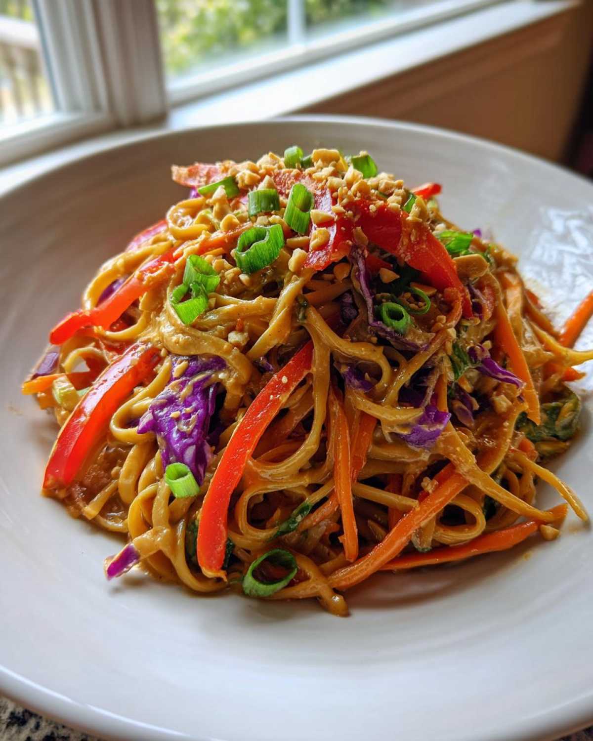 A bowl of Thai Peanut Noodles with Crunchy Veggies, topped with chopped peanuts and scallions.