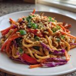 A close-up of a serving of Thai Peanut Noodles with Crunchy Veggies, topped with crushed peanuts and green onions.