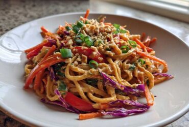A close-up of a serving of Thai Peanut Noodles with Crunchy Veggies, topped with crushed peanuts and green onions.