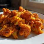 Close-up of roasted cauliflower florets coated in a rich, orange-red sauce for Vegan Cauliflower Tikka Masala.