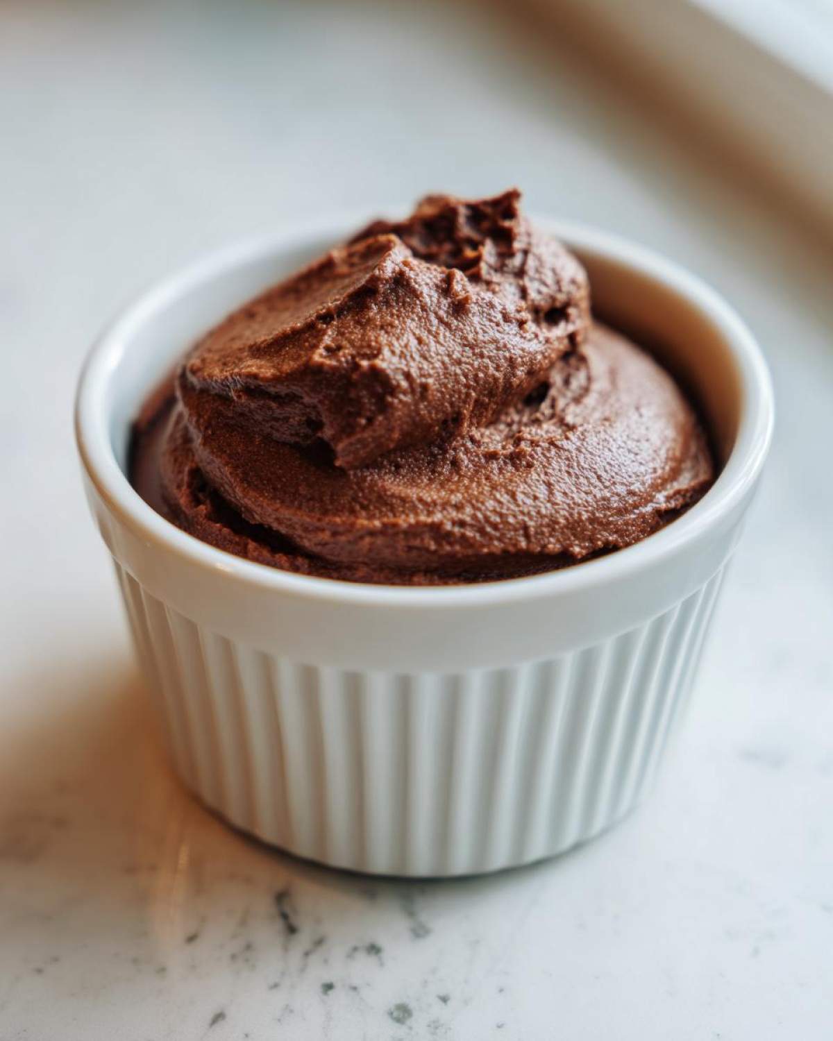 A close-up of rich, dark Vegan Chocolate Avocado Mousse swirled high in a white, ribbed ramekin.