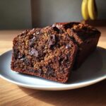 Two moist slices of Vegan Chocolate Banana Bread loaded with melted chocolate chips on a white plate.