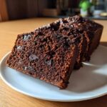 Close-up of thick slices of moist Vegan Chocolate Banana Bread with visible chocolate chips on a white plate.