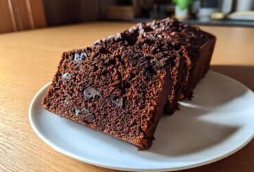 Close-up of thick slices of moist Vegan Chocolate Banana Bread with visible chocolate chips on a white plate.
