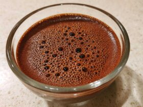 Close-up of rich, dark brown Vegan Chocolate Chia Pudding mixture with small bubbles on top in a clear glass bowl.