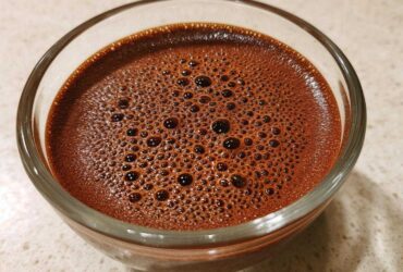 Close-up of rich, dark brown Vegan Chocolate Chia Pudding mixture with small bubbles on top in a clear glass bowl.