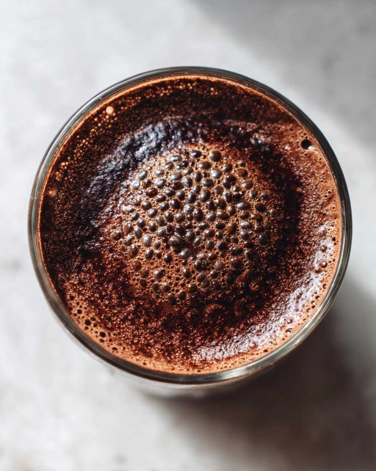 Overhead close-up of rich, dark Vegan Chocolate Chia Pudding with a layer of fine bubbles on top.