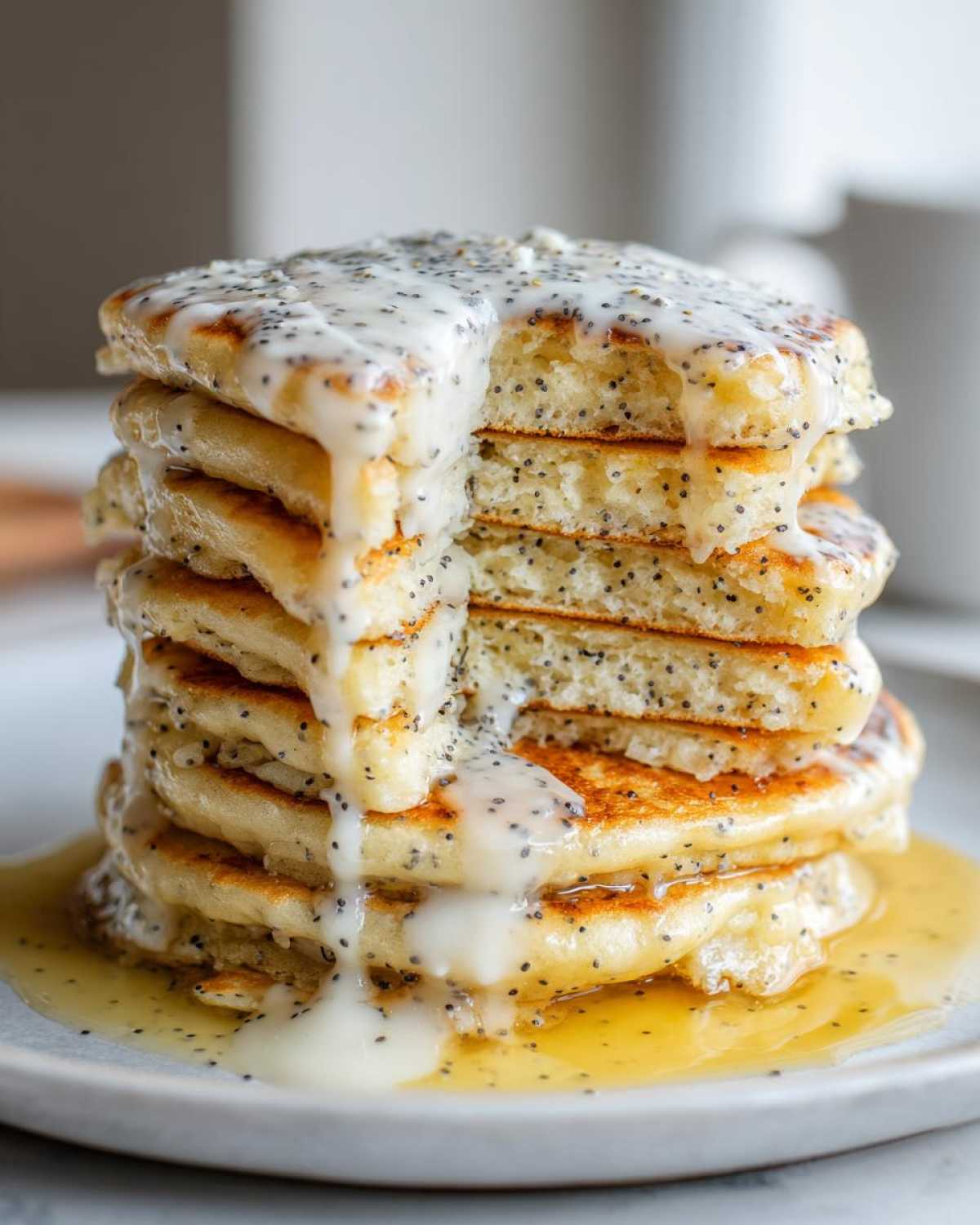 A tall stack of fluffy Vegan Lemon Poppy Seed Pancakes dripping with a thick lemon glaze and poppy seeds.