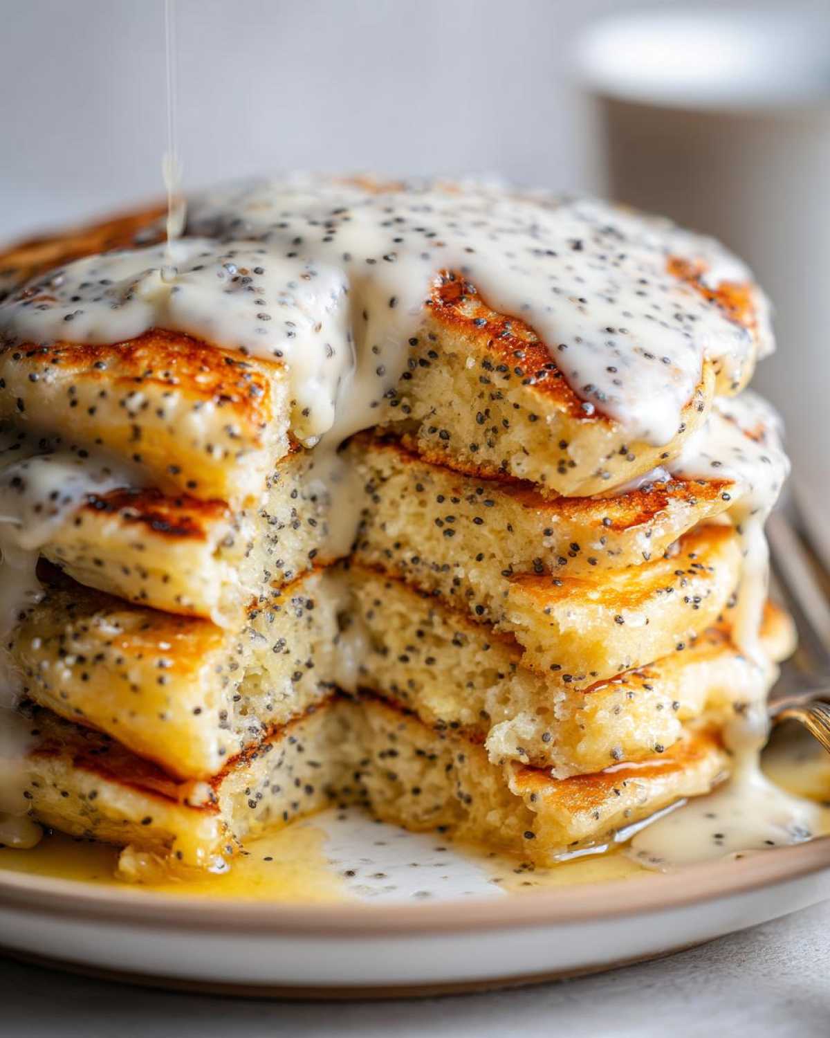 Close-up of a stack of fluffy Vegan Lemon Poppy Seed Pancakes drizzled with a thick lemon glaze.
