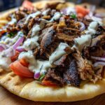Close-up of Vegan Mushroom Shawarma piled high with savory mushrooms, tomatoes, red onion, and drizzled with white sauce on pita bread.