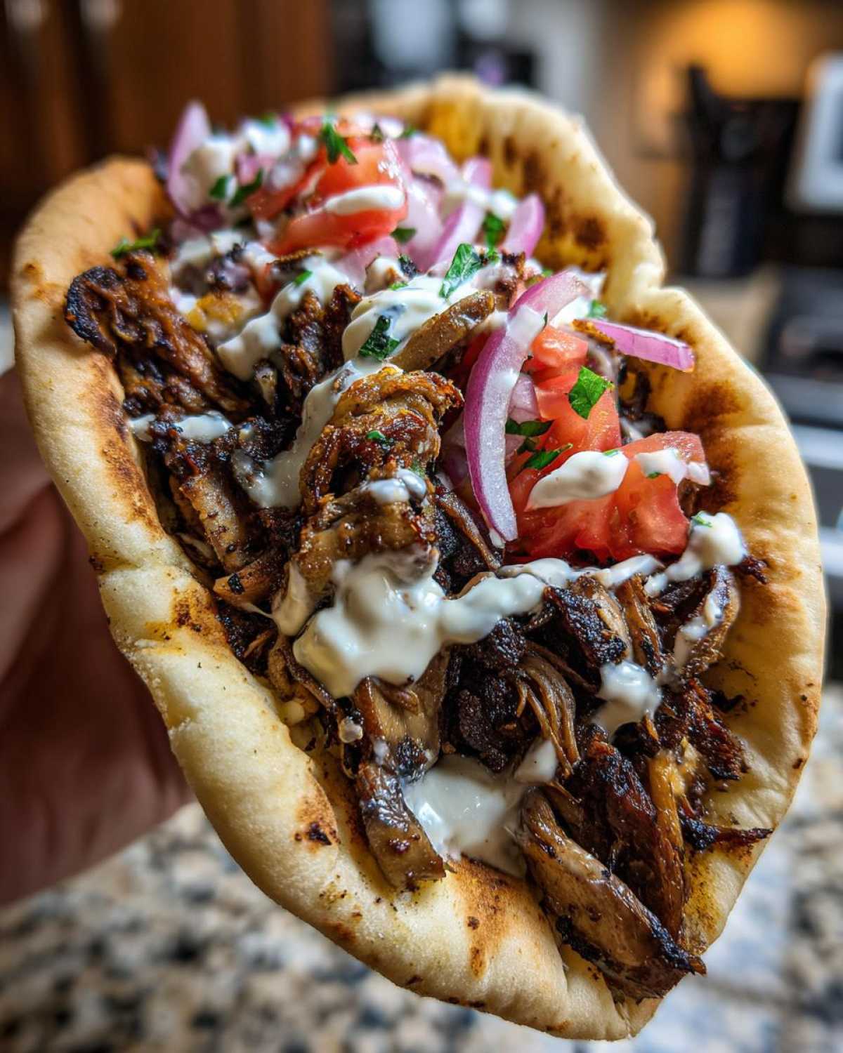 Close-up of a handheld Vegan Mushroom Shawarma stuffed with seasoned mushrooms, tomatoes, red onion, and drizzled with white sauce.
