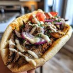 Close-up of a loaded pita bread filled with Vegan Mushroom Shawarma, tahini sauce, red onion, and tomato.