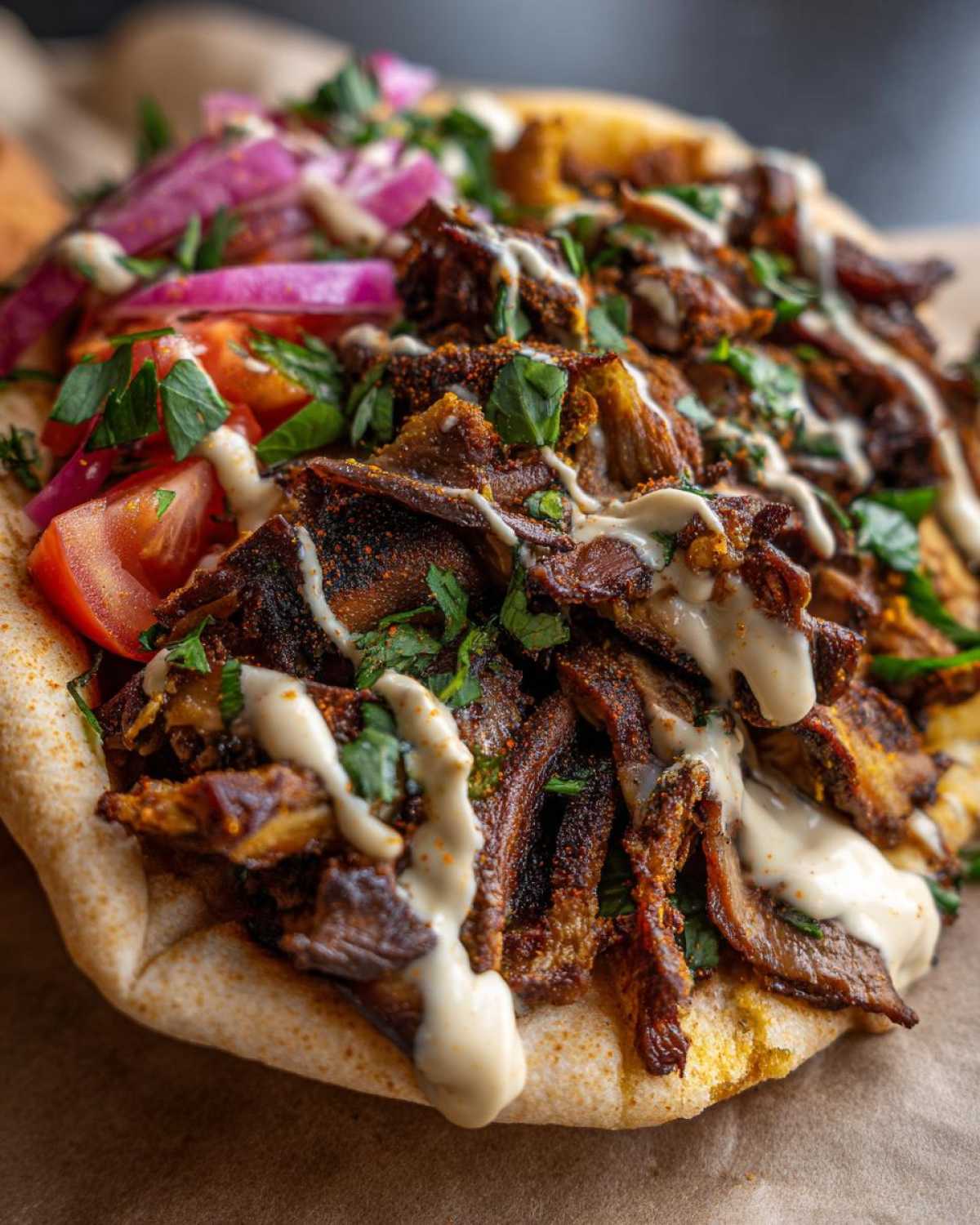 Close-up of seasoned Vegan Mushroom Shawarma piled high on pita bread, drizzled with tahini sauce and topped with fresh tomatoes and onions.