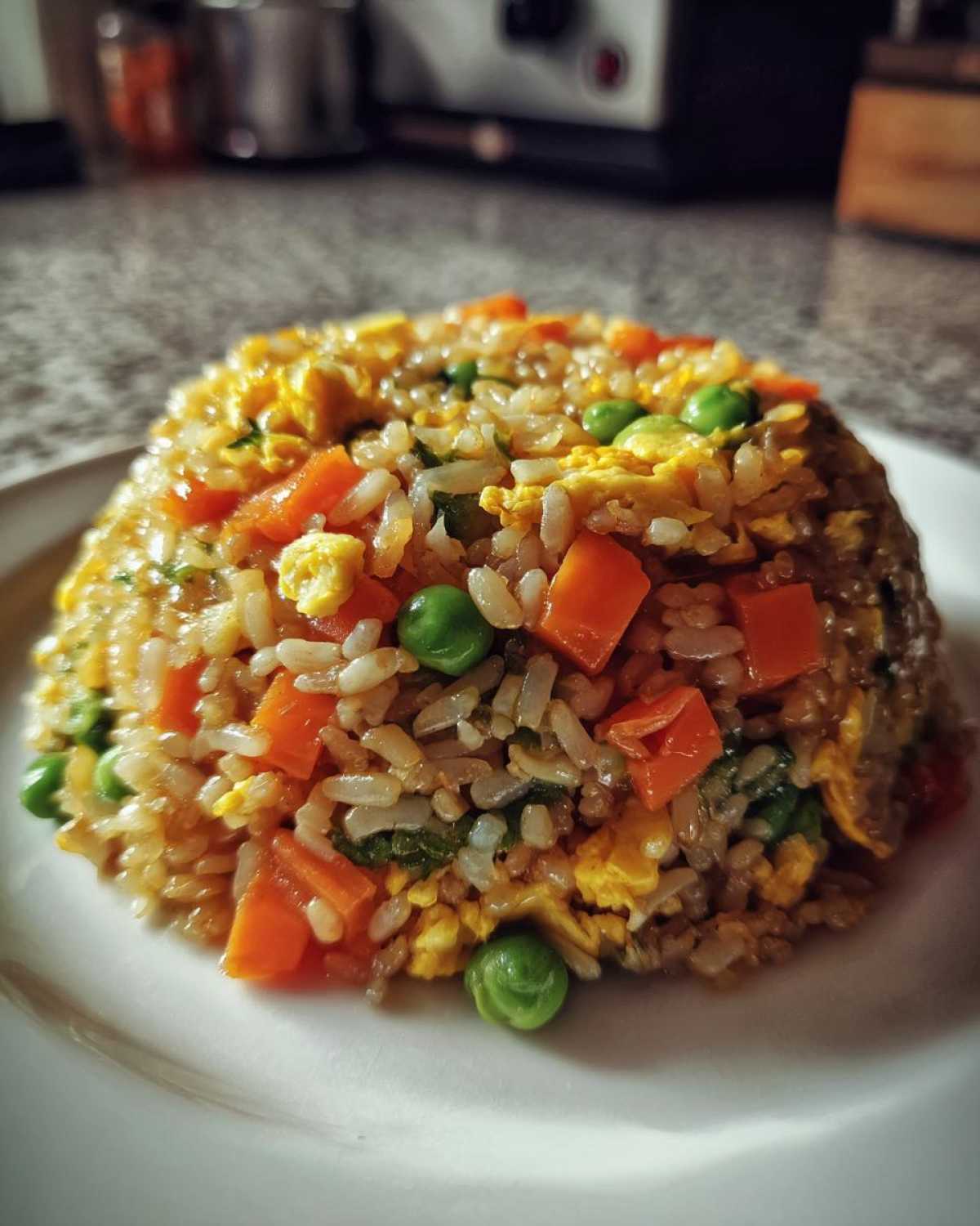 A close-up of a perfectly molded serving of Vegetable Fried Rice with visible carrots, peas, and scrambled egg.