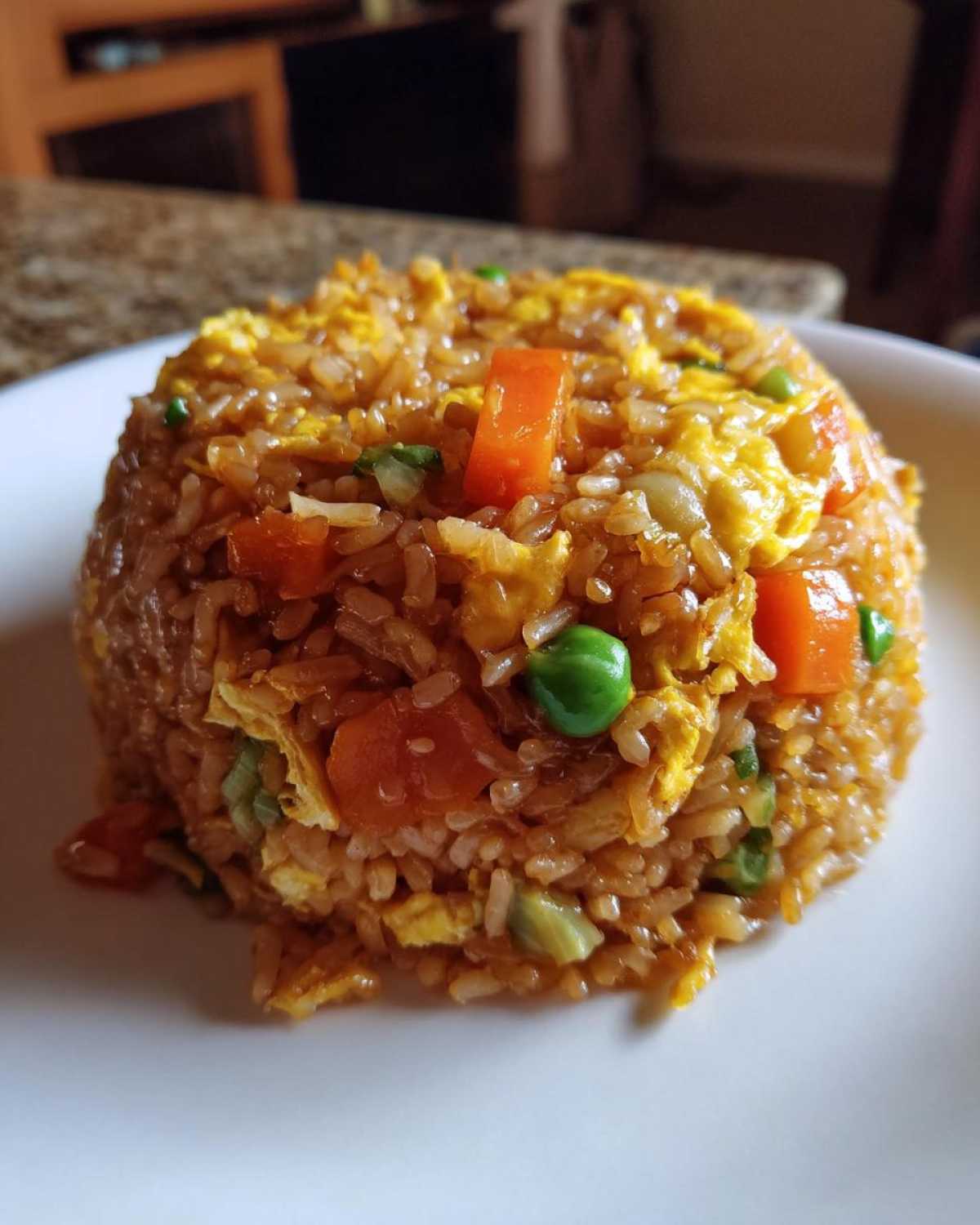 A close-up of a perfectly molded serving of Vegetable Fried Rice with visible pieces of scrambled egg, carrots, and peas.