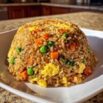 A dome-shaped serving of Vegetable Fried Rice with Sesame Ginger Sauce, featuring visible carrots, peas, and scrambled egg pieces.