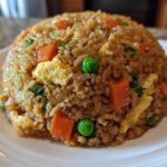 A dome-shaped serving of Vegetable Fried Rice with Sesame Ginger Sauce, featuring visible carrots, peas, and scrambled egg pieces.