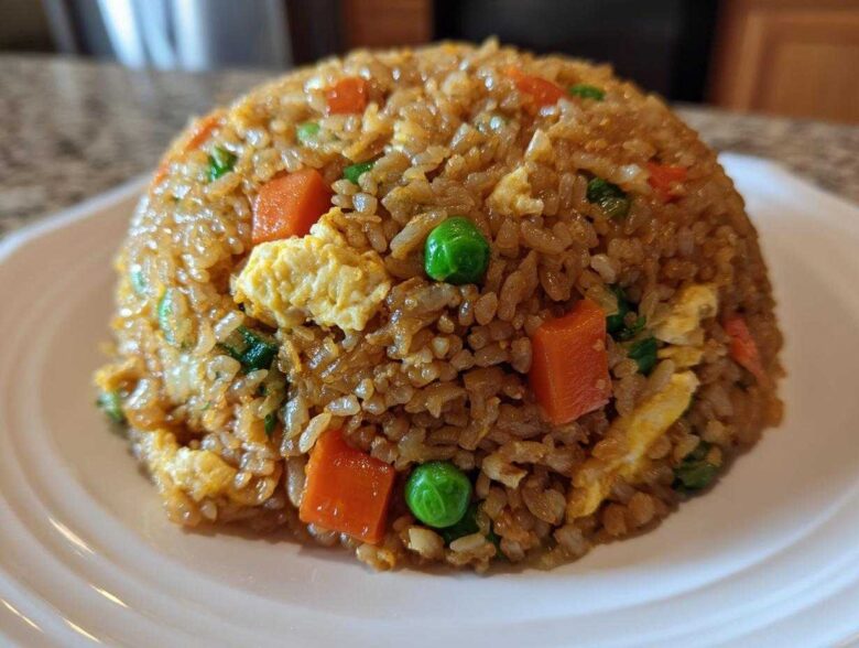 A dome-shaped serving of Vegetable Fried Rice with Sesame Ginger Sauce, featuring visible carrots, peas, and scrambled egg pieces.