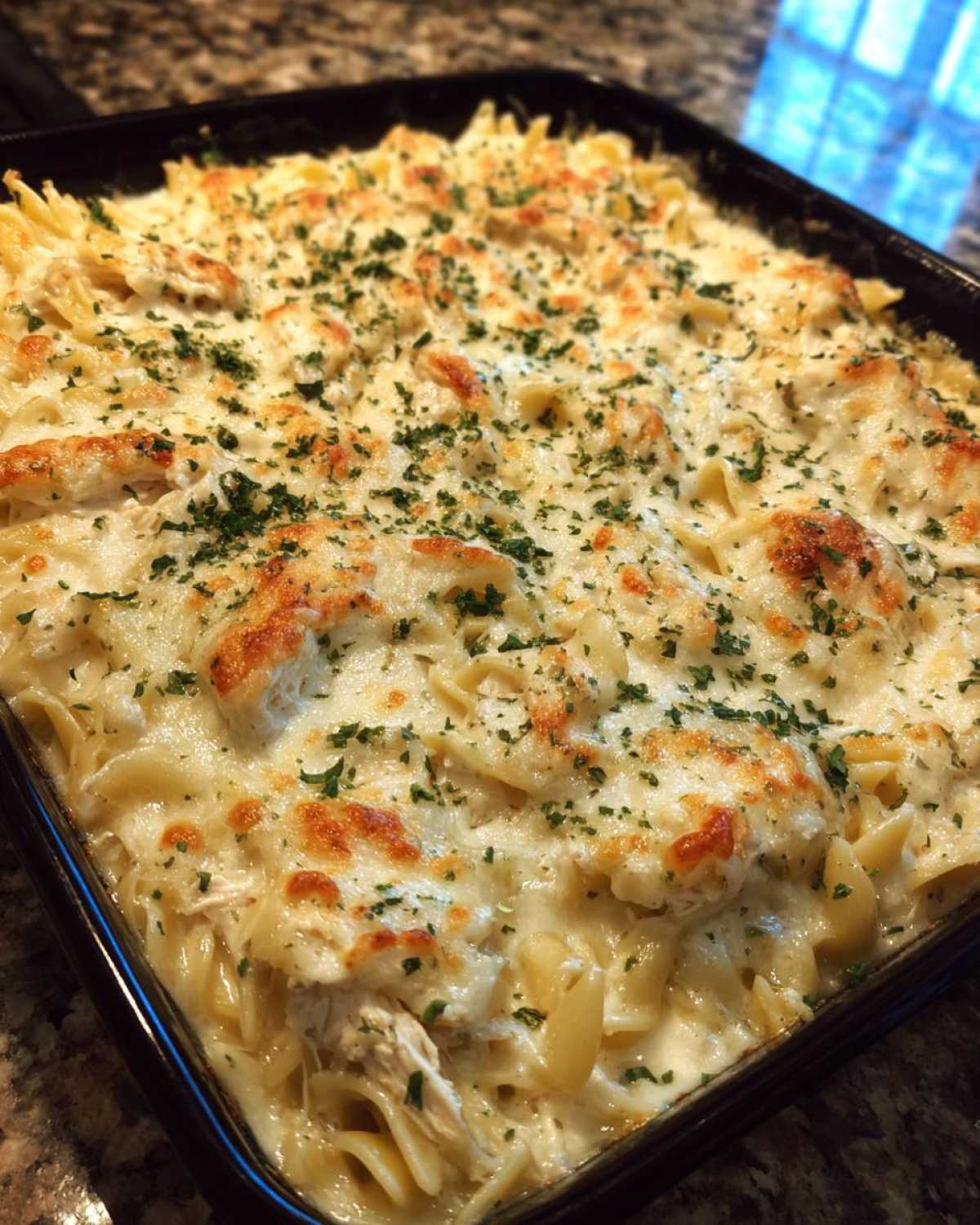 A close-up of a bubbling Cheesy Chicken Alfredo Bake with Mozzarella, topped with melted cheese and fresh parsley.