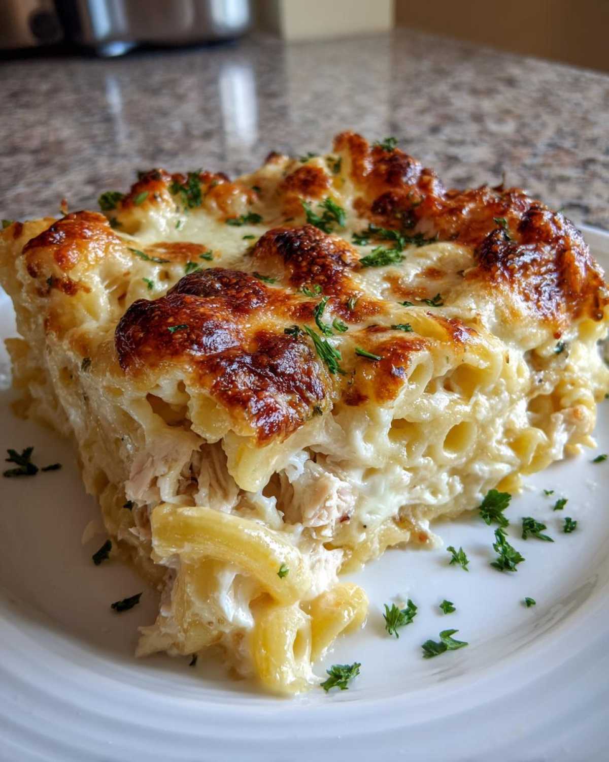 A rich, golden-brown slice of Cheesy Chicken Alfredo Bake with Mozzarella, topped with melted, bubbly cheese and parsley.