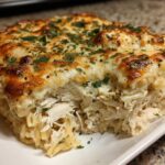 A thick slice of Cheesy Chicken Alfredo Bake with Mozzarella showing shredded chicken and pasta under a golden, bubbly cheese topping.