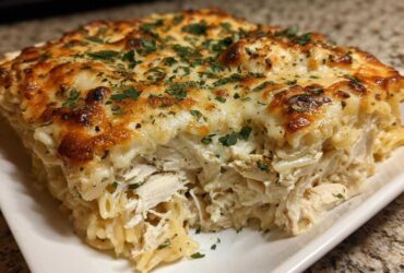 A thick slice of Cheesy Chicken Alfredo Bake with Mozzarella showing shredded chicken and pasta under a golden, bubbly cheese topping.