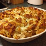 A close-up of a white baking dish filled with Cheesy Chicken Pasta with Creamy Sauce, featuring a bubbly, browned cheese crust.
