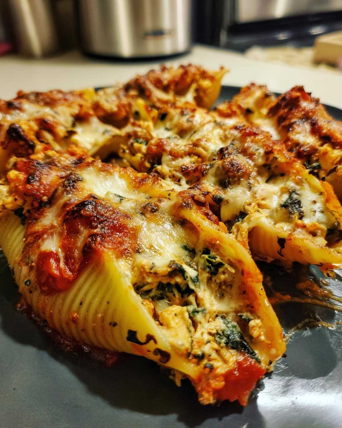 Close-up of baked Cheesy Chicken Stuffed Shells with Spinach topped with melted, browned mozzarella cheese and tomato sauce.