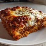 A square serving of Cheesy Ground Beef Pasta Bake, featuring layers of pasta, meat sauce, and melted, browned cheese on top.