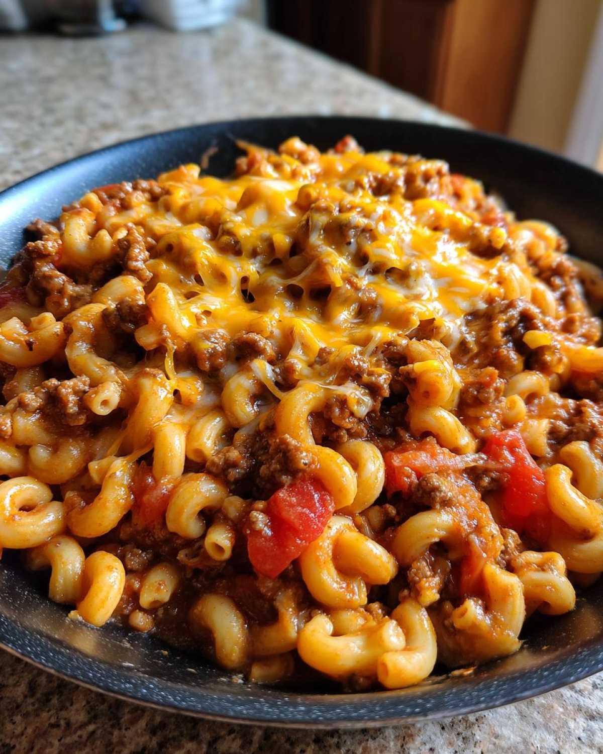 Close-up of Cheesy Ground Beef Pasta Skillet Comfort Food with melted cheddar cheese over elbow macaroni and meat sauce.
