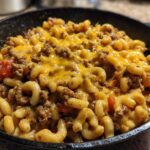Close-up of Cheesy Ground Beef Pasta Skillet Comfort Food topped with melted cheddar cheese in a cast iron pan.