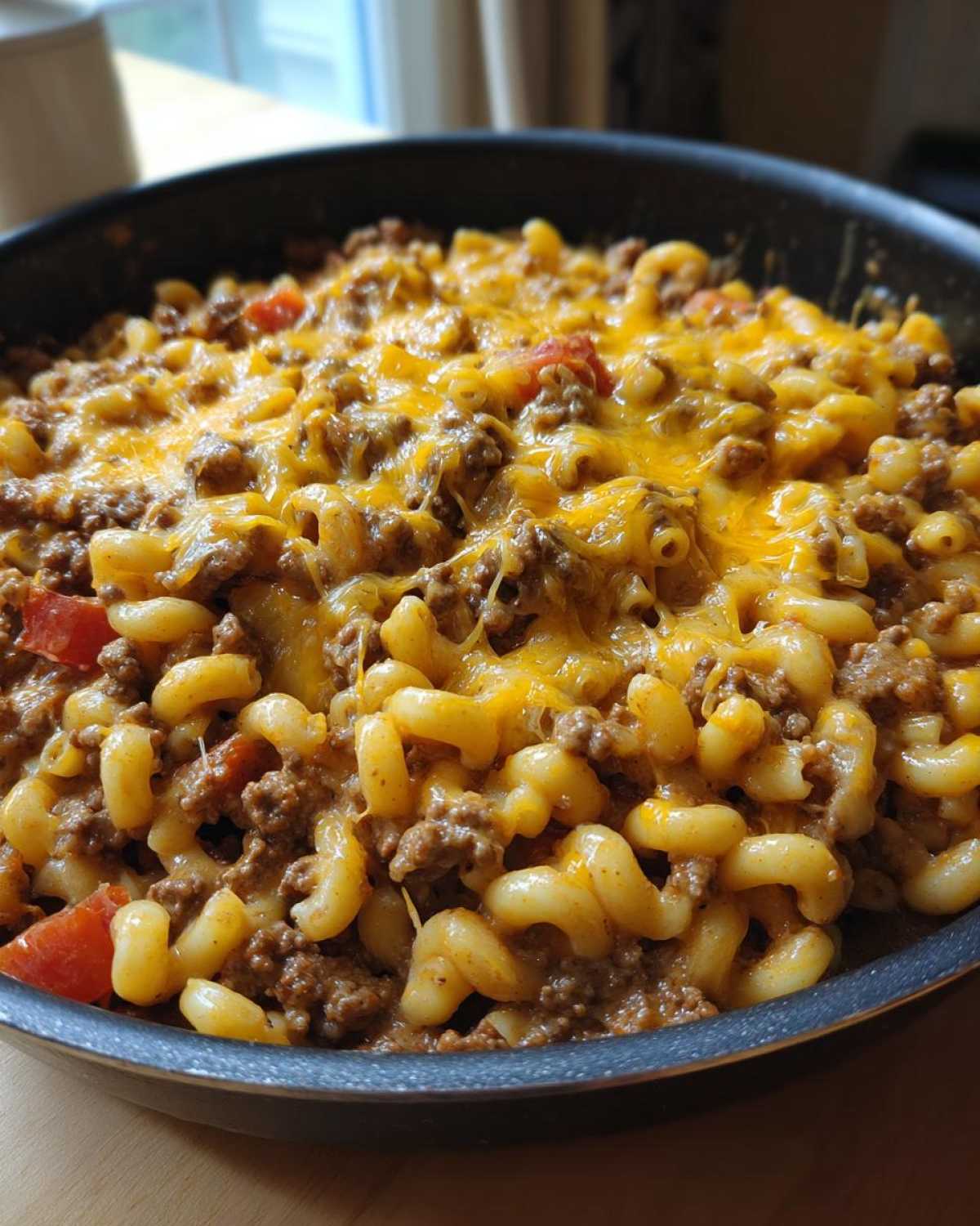 Close-up of Cheesy Ground Beef Pasta Skillet Comfort Food topped with melted cheddar cheese in a black skillet.