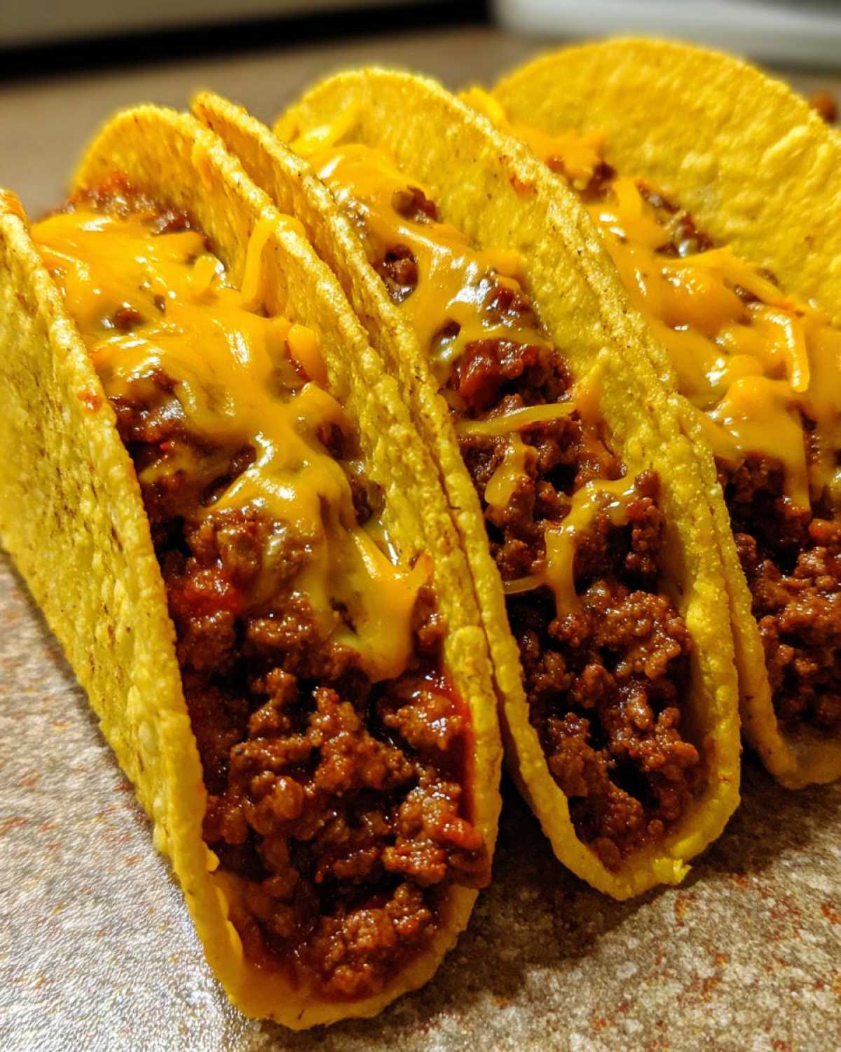 Three hard-shell tacos filled with seasoned ground beef and melted cheddar cheese, ready to eat for Cheesy Ground Beef Tacos.