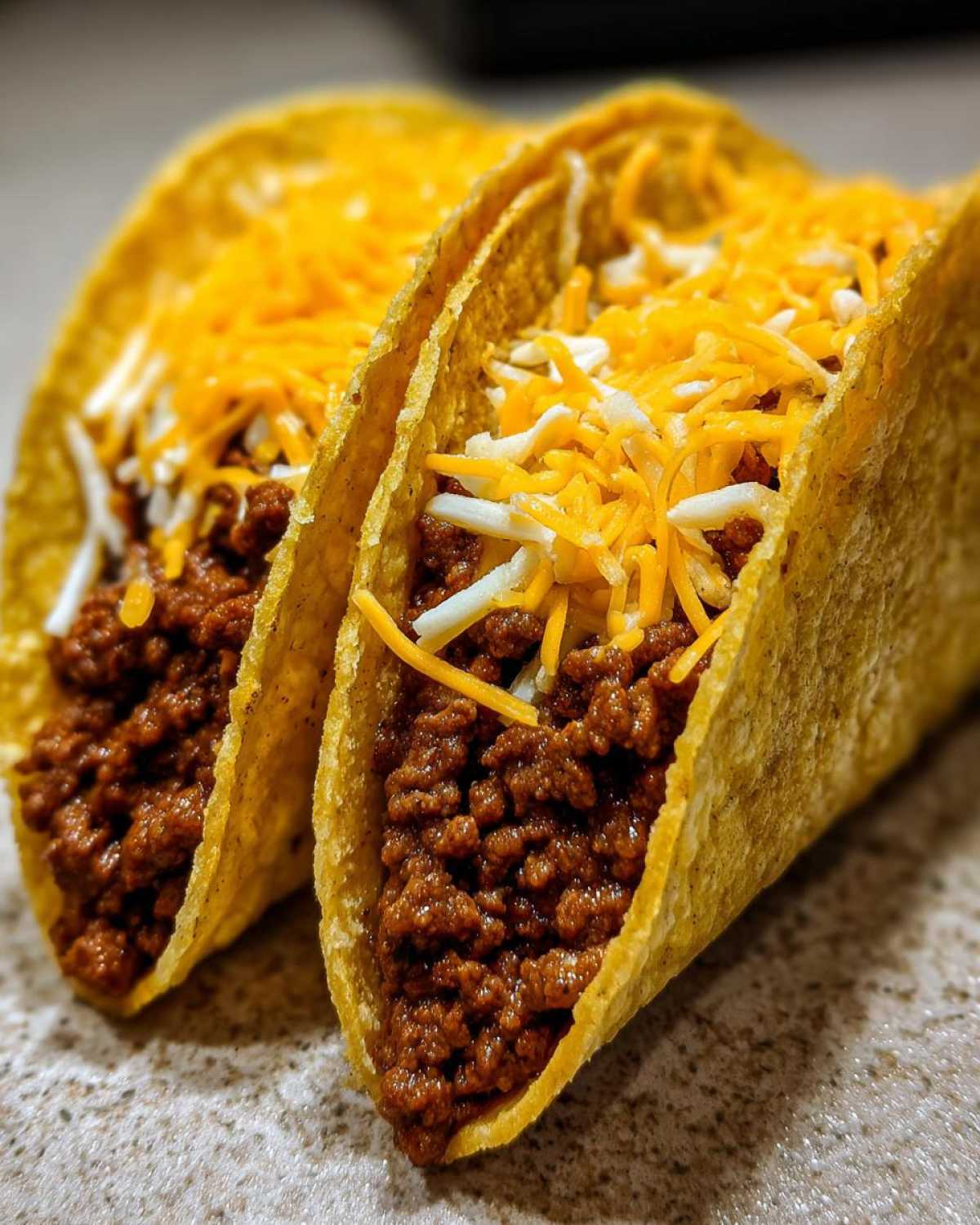 Two crispy tacos filled with seasoned ground beef and topped generously with shredded cheddar and Monterey Jack cheese, showcasing the Cheesy Ground Beef Tacos.
